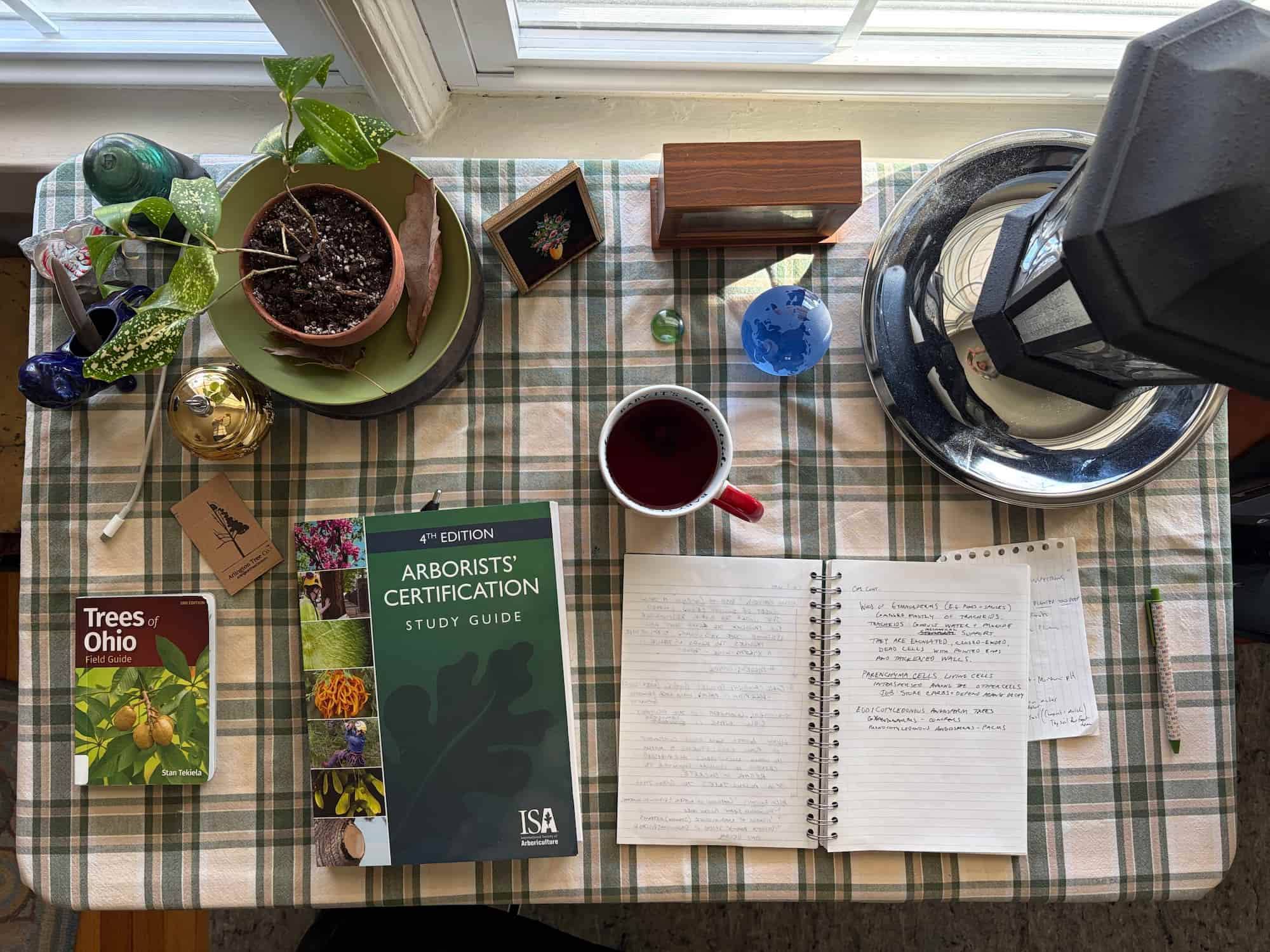 The ISA Arborists' Certification Study Guide open on a desk beside a notebook of handwritten notes, with ArbKeep on a laptop